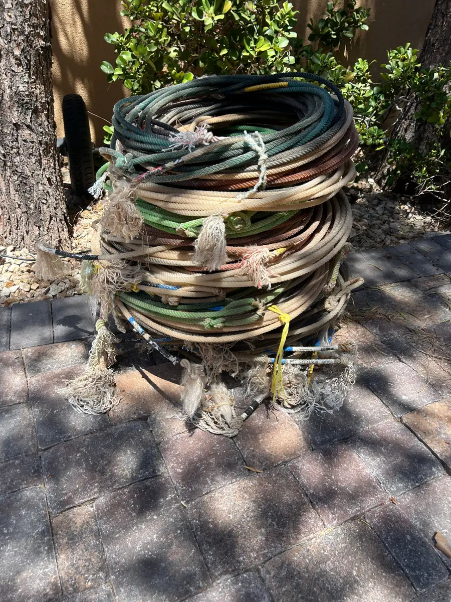 Coiled stack of used rodeo lariat ropes in earthy greens, browns, and naturals